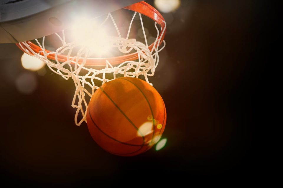 Basketball entering hoop with bright background.