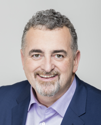 A man with grey hair and a beard wearing a suit.