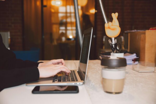 Close-up of hands typing on a laptop in a modern office setting with coffee and creative decor.